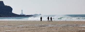 Walkers lighthouse beach waves This landscape photograph captures a coastal scene at Sennen Cove, Cornwall, United Kingdom, during a spring afternoon. The image prominently features Walkers lighthouse on the rugged coastline, with gentle waves rolling onto the sandy beach. Several people are visible walking along the shoreline, highlighting the interaction between nature and leisure activity. The blue sea and the rocky outcrops frame the lighthouse, serving as a recognizable landmark within the composition. The photograph showcases the natural beauty of the Cornish coast, illustrating both the peacefulness of the beach and the presence of human activity.